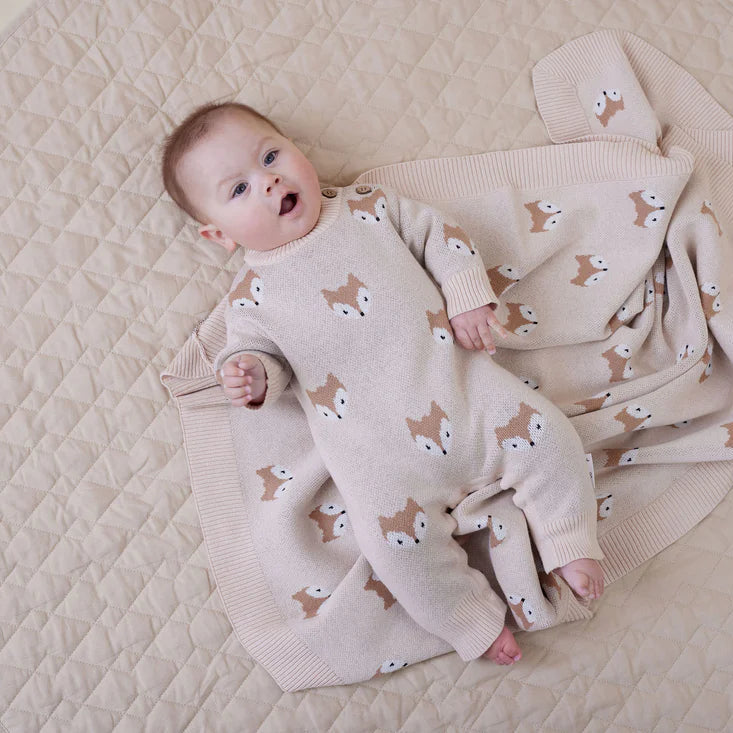 Baby lying on a quilted play mat wearing a white onesie with animal patterns.