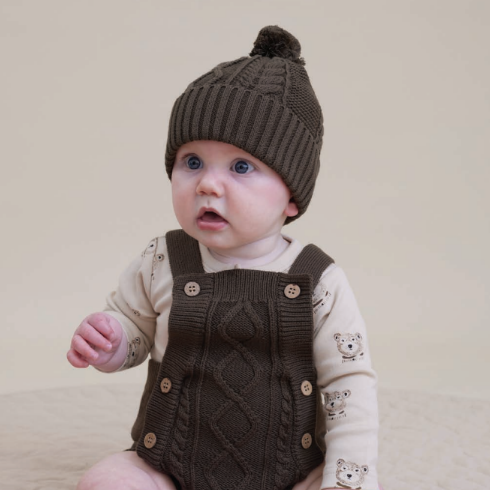 Baby wearing a brown knit outfit with a matching hat on a plain background