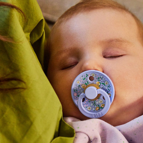 Baby sucking a BIBS Liberty printed pacifier sold by Meridian Baby.
