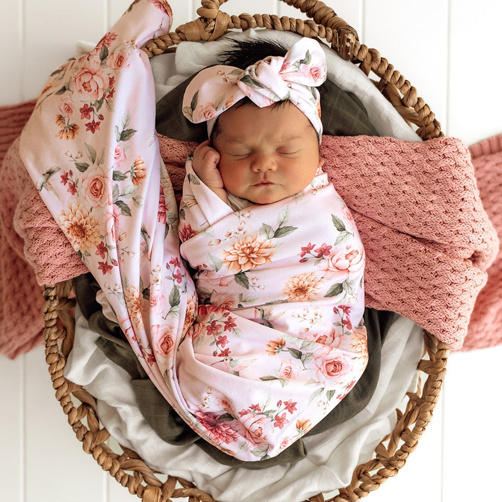 Newborn baby girl wrapped in Snuggle Hunny pink floral wrap with matching headband from Meridian Baby
