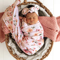 Newborn baby girl wrapped in Snuggle Hunny pink floral wrap with matching headband from Meridian Baby