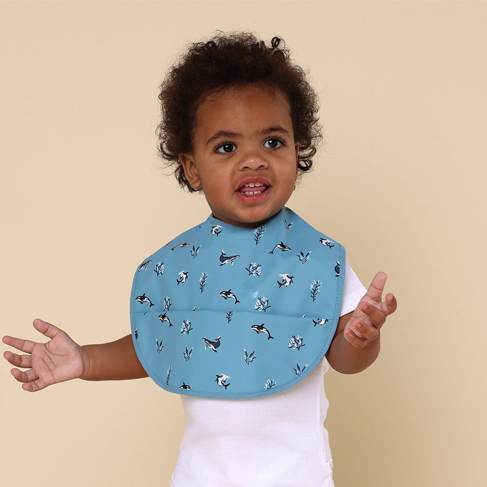 Toddler wearing Snuggle Hunny blue ocean feeding bib from Meridian Baby