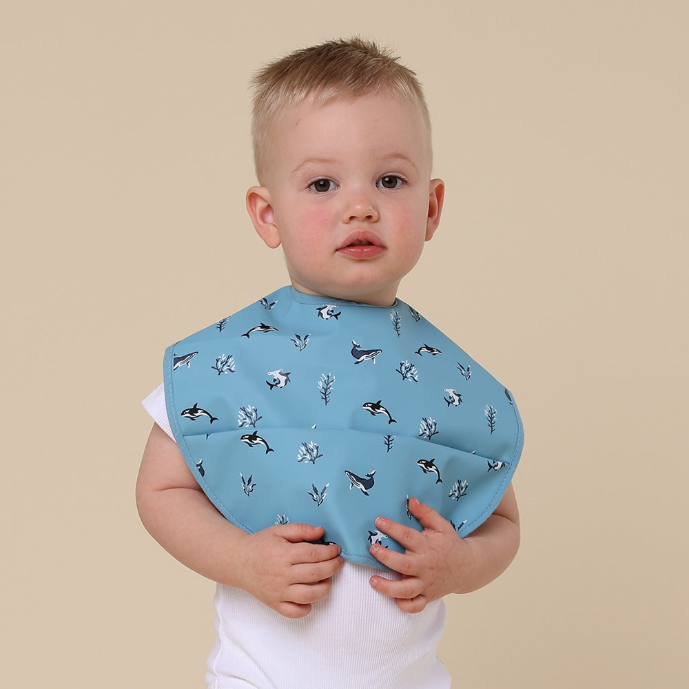 Toddler wearing Snuggle Hunny blue ocean snuggle bib from Meridian Baby