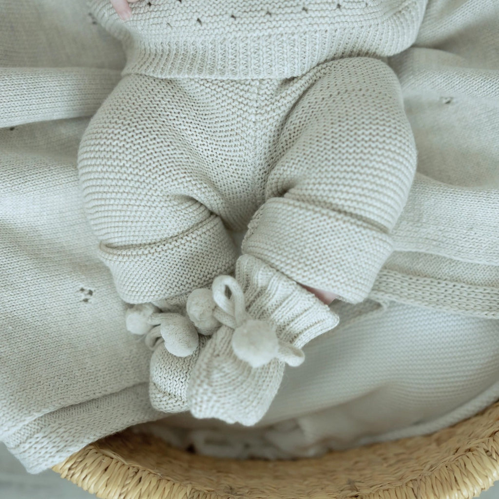 Knitted baby outfit with pants and booties on a textured surface