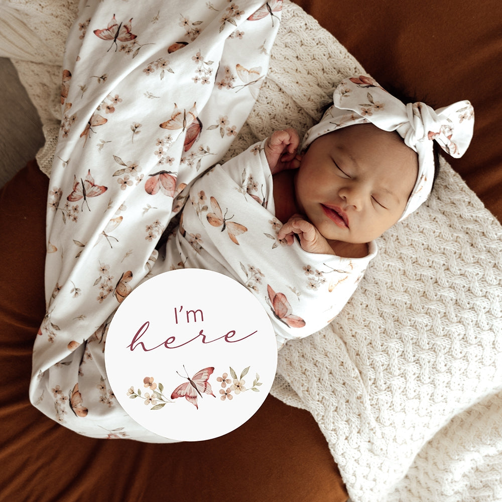 Newborn baby wrapped in a floral swaddle with a matching headband, lying on a textured surface.