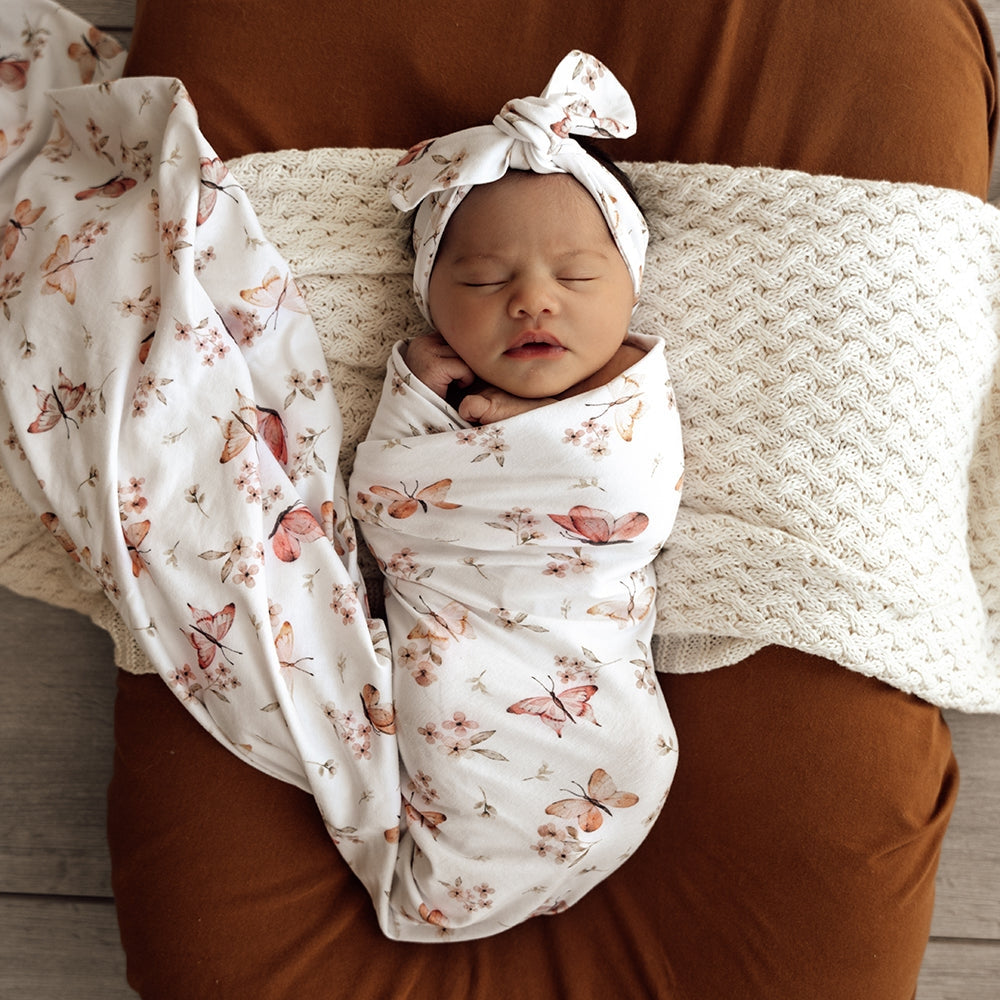 Newborn baby swaddled in a floral blanket with butterfly pattern, wearing a matching headband.