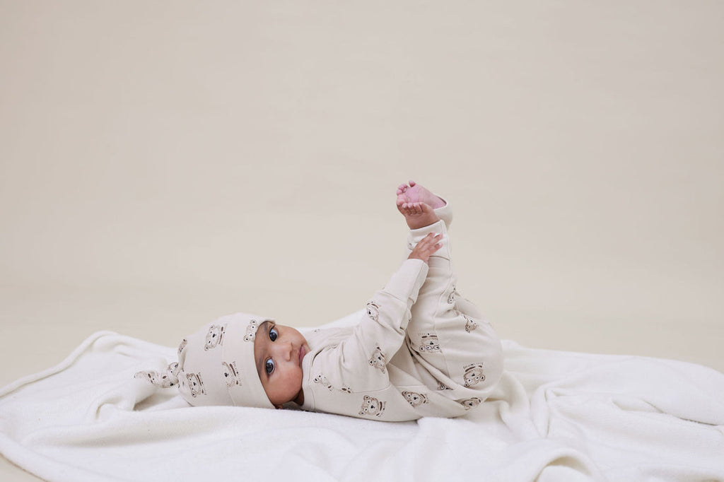 Baby lying on a white blanket wearing a matching outfit and hat.