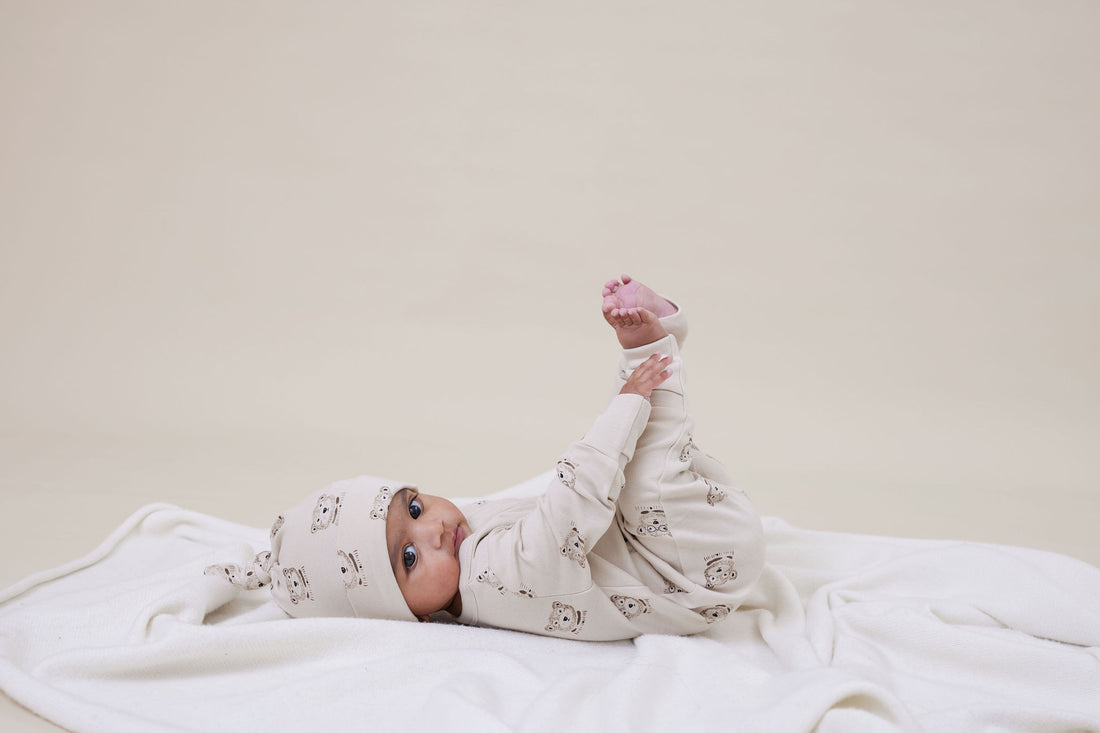 Baby lying on a white blanket wearing a matching outfit and hat.