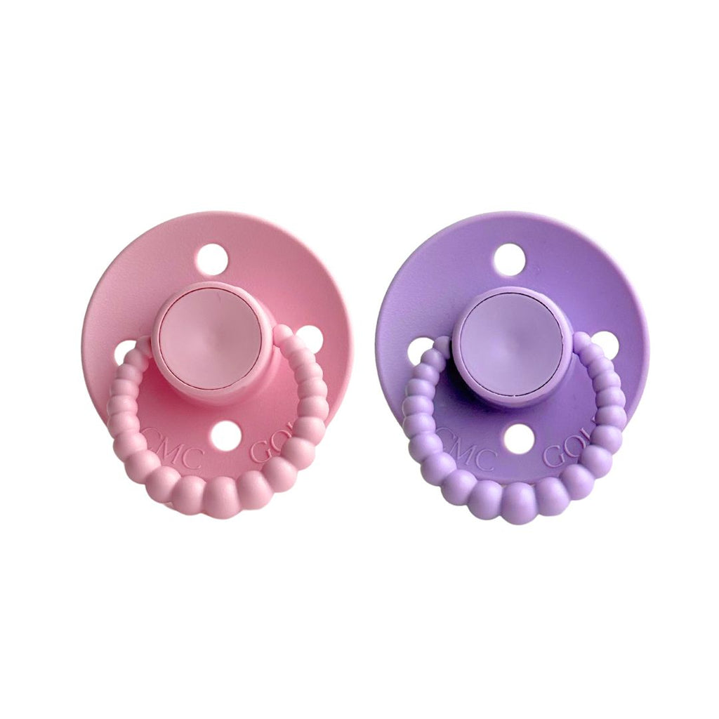 Two baby pacifiers, one pink and one purple, on a white background.