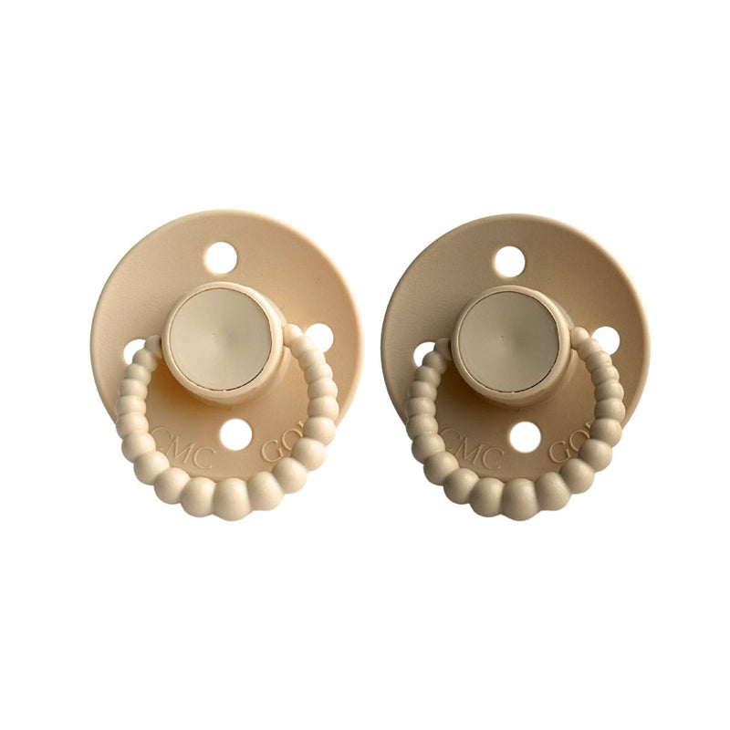 Two beige pacifiers with bead details on a white background