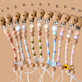 Set of wooden pacifier clips with colorful beads and charms on a beige background