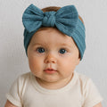 Baby wearing a blue headband with a bow on a plain background
