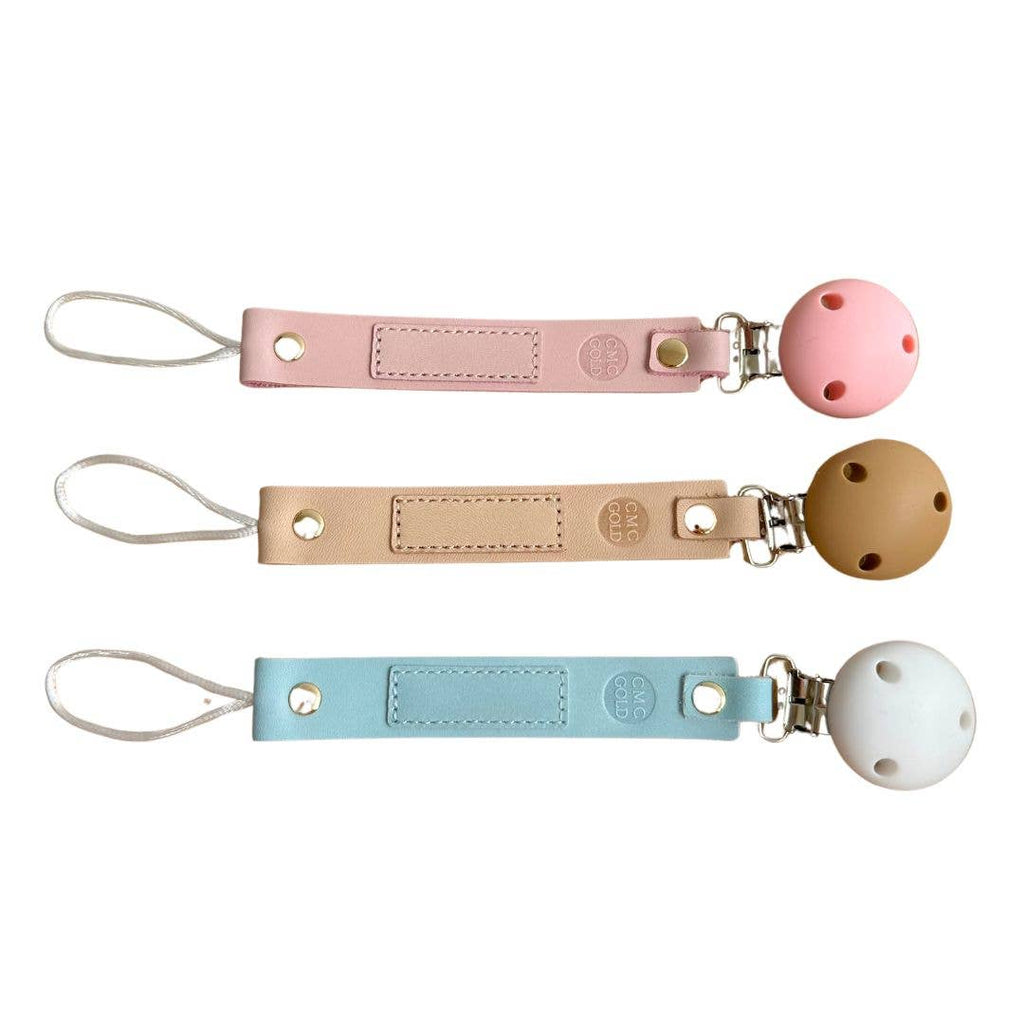 Three CMC Gold pacifier clips with different colored straps sold by Meridian Baby