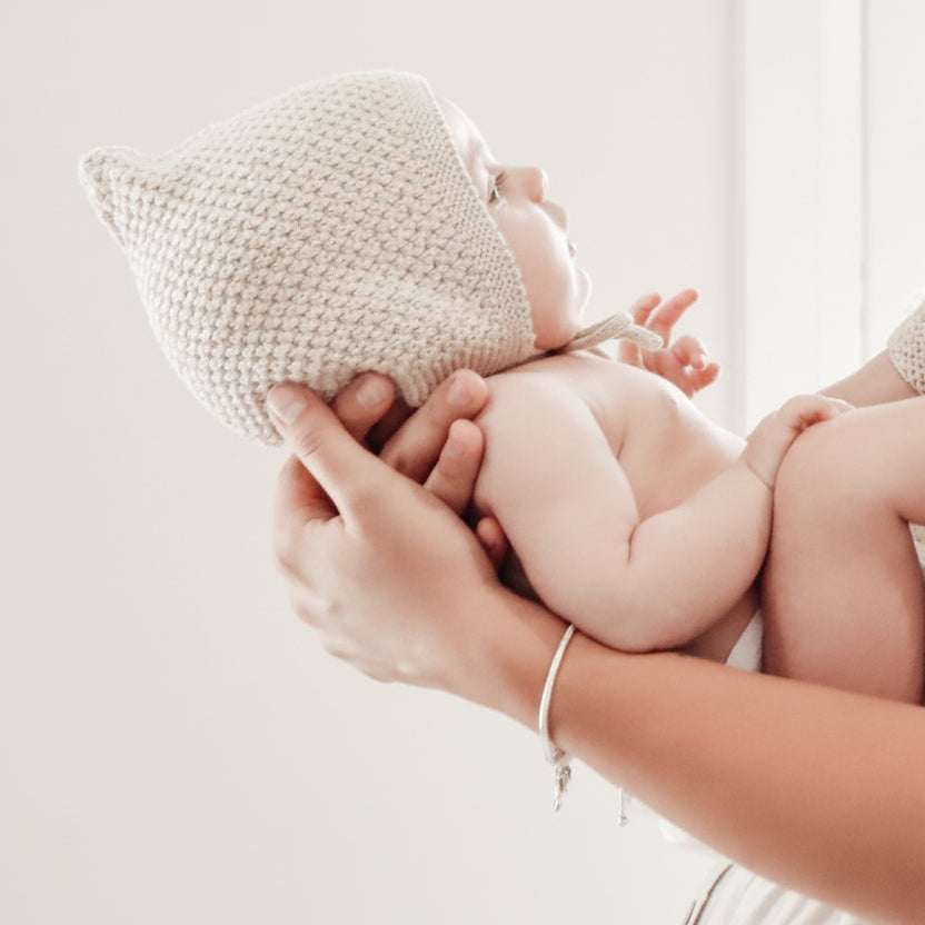 Baby wearing a knitted hat being held by a person against a light background