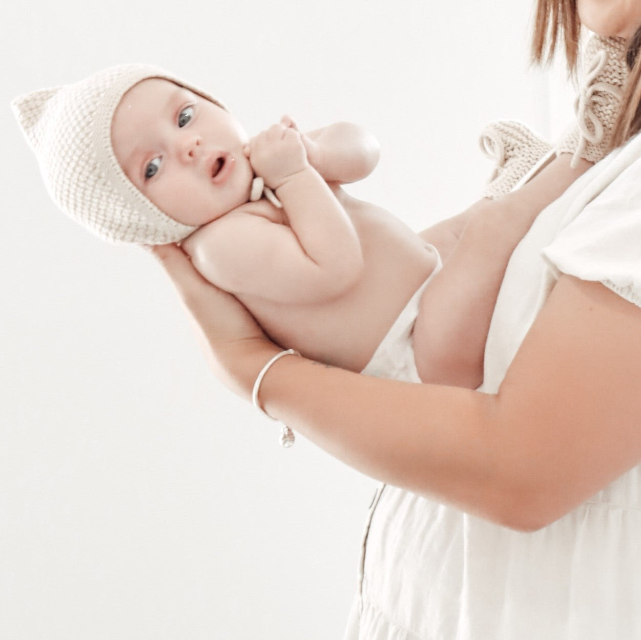 Baby being held by a person wearing a white outfit on a light background