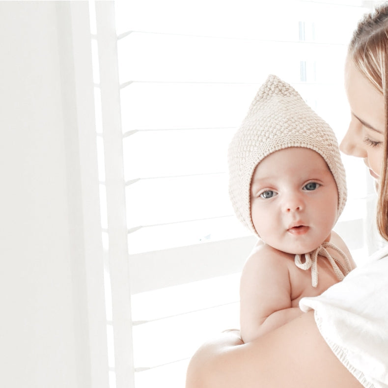 Woman holding a baby in a white outfit with a light background