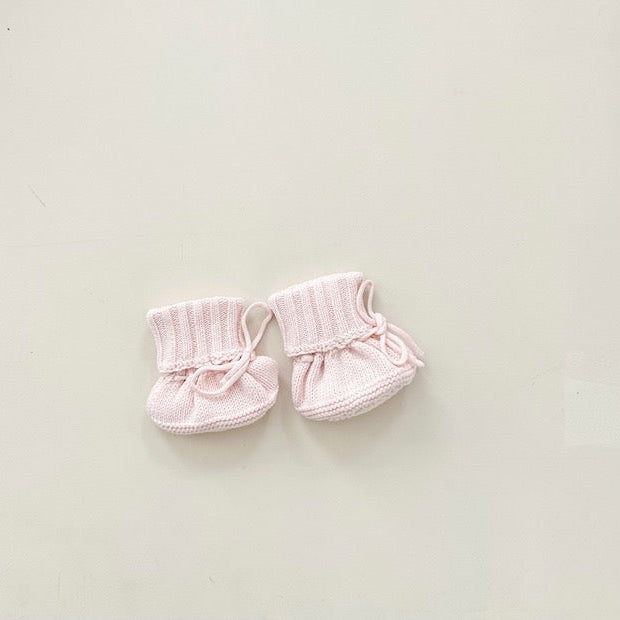 Pair of pink baby booties on a light beige background