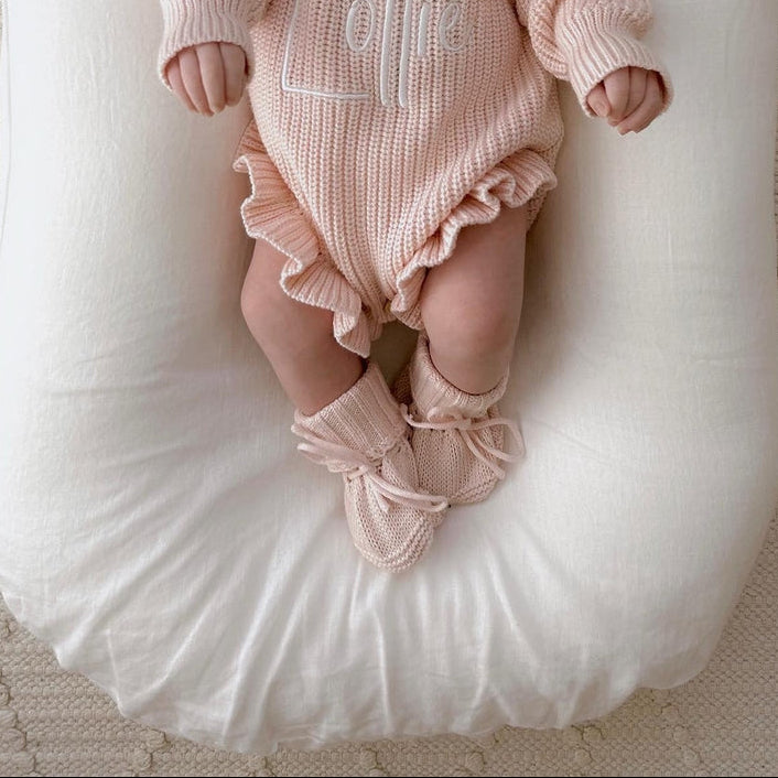 Newborn baby in a pink outfit lying on a white crib