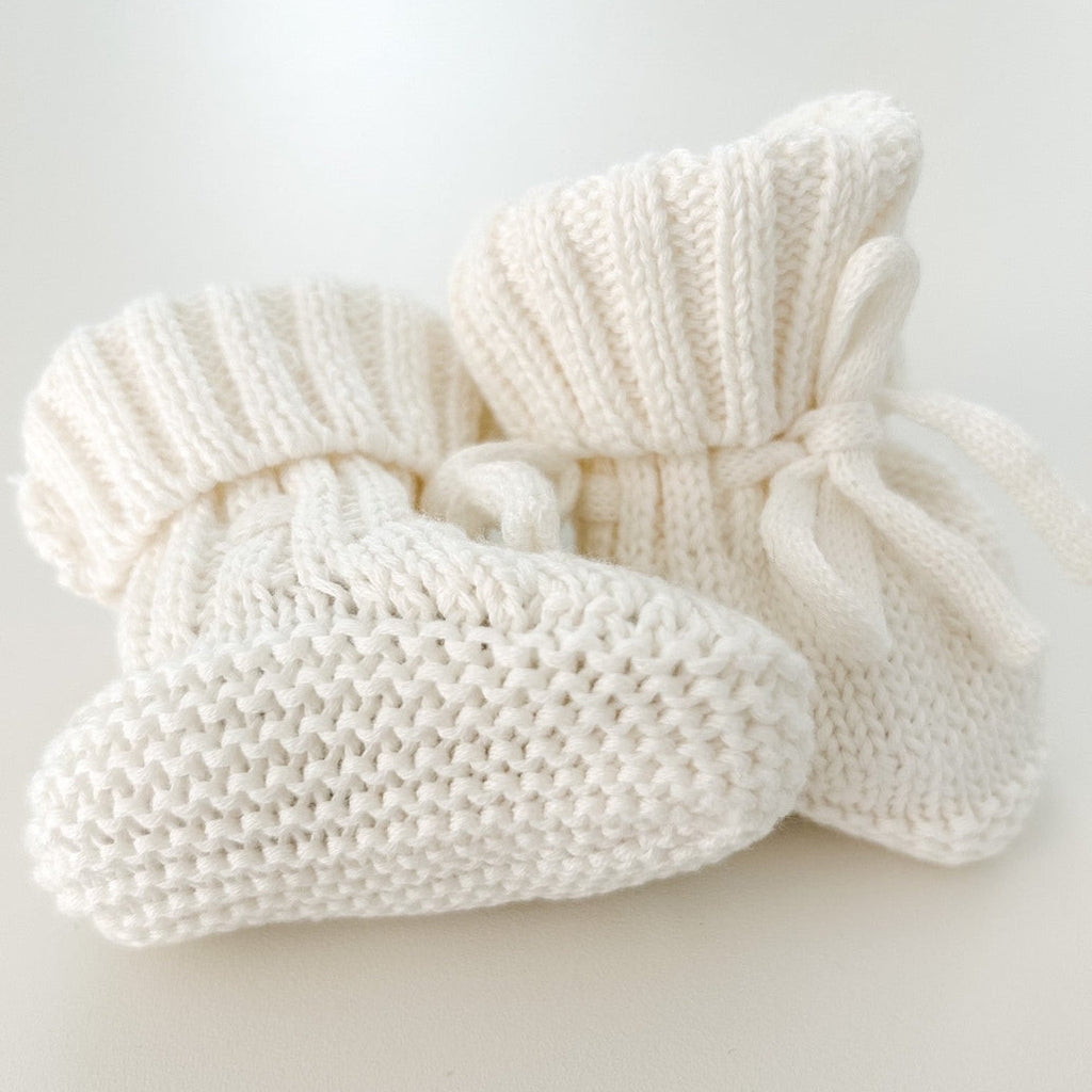 Pair of white knitted baby booties on a light gray background