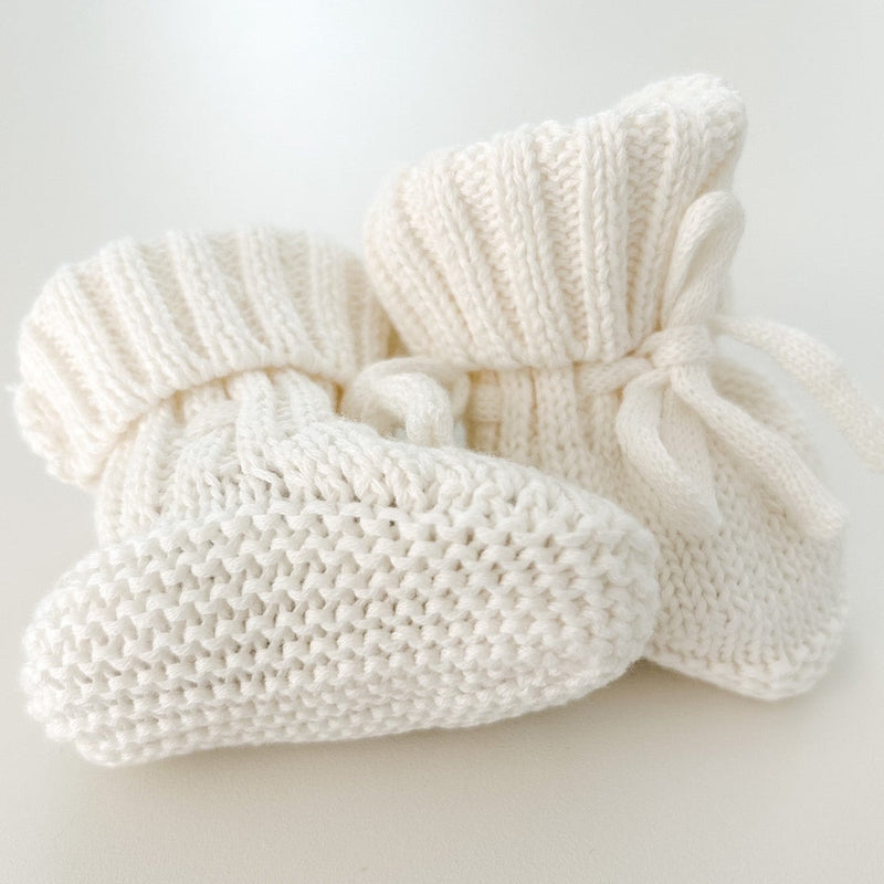 Pair of white knitted baby booties on a light gray background