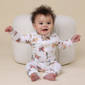 Baby wearing a floral onesie sitting on a beige chair.