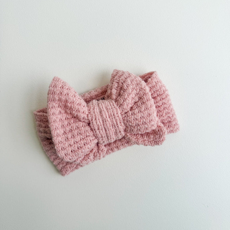 Pink knitted headband with a bow on a light gray background