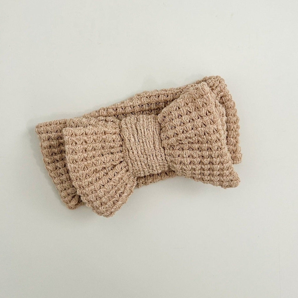 Brown knitted headband with a bow on a light gray background