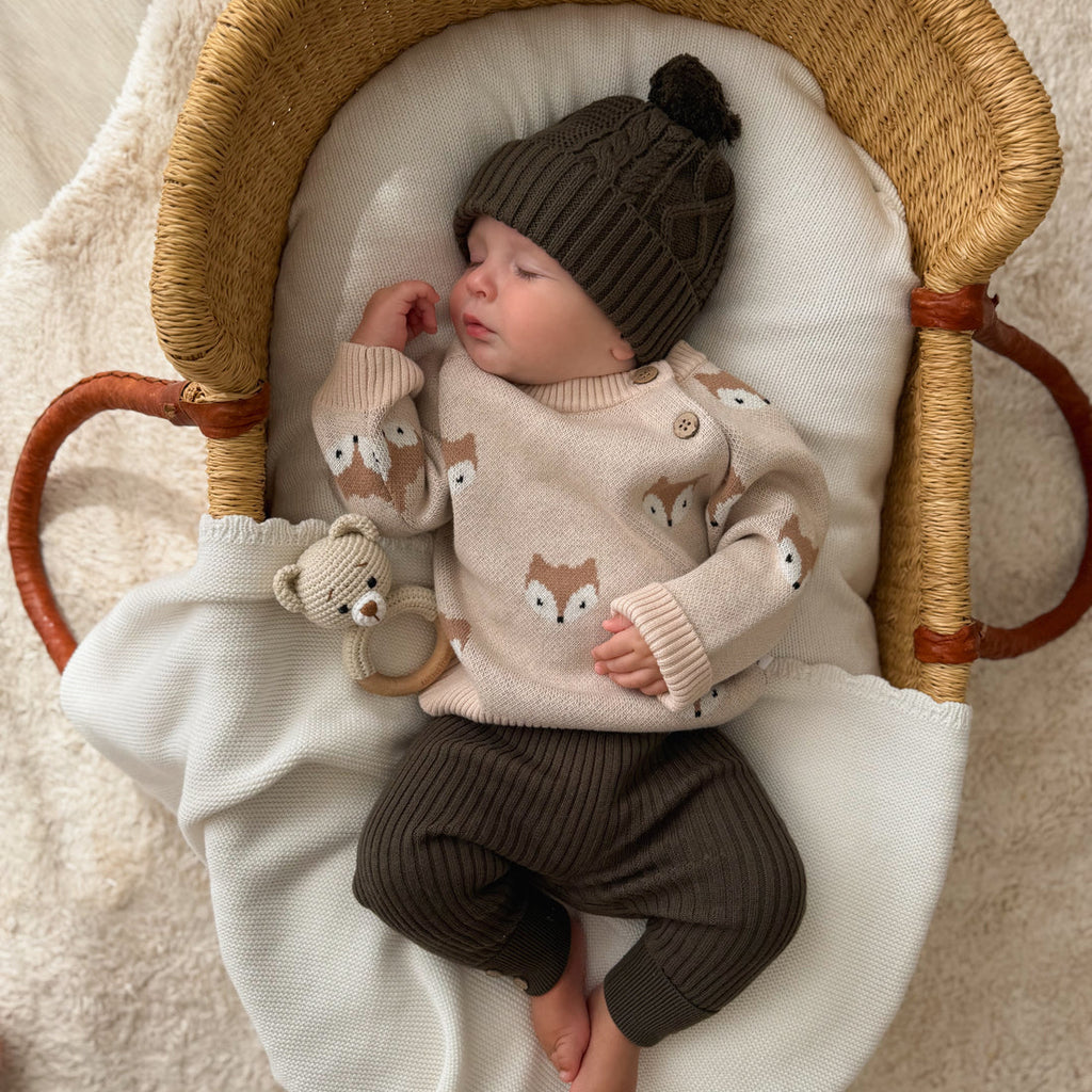 Newborn baby in a Moses basket wearing an Aster & Oak tan fox sweater and brown ribbed leggings from Meridian Baby