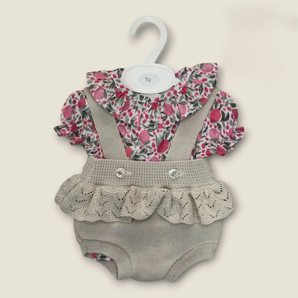 Baby romper with floral top and ruffled skirt on a hanger against a beige background