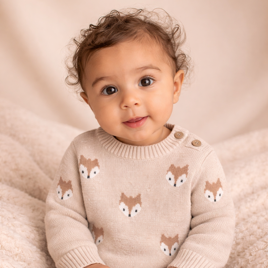 Baby wearing a beige sweater with fox patterns on a soft beige background