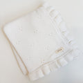 White knitted blanket with ruffle edge on a light background