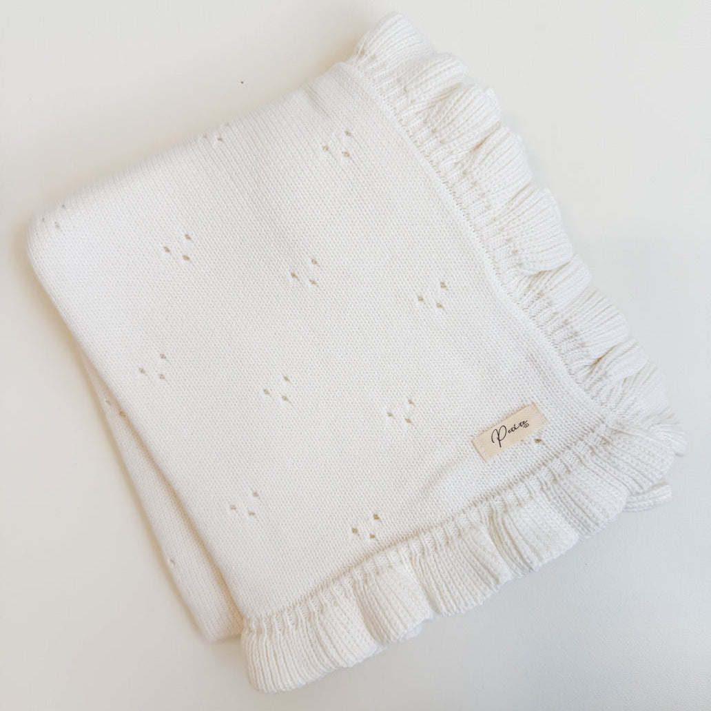White knitted blanket with ruffle edge on a light background