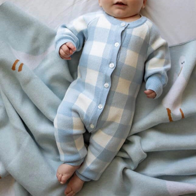 Baby in a blue and white checkered outfit lying on a soft blanket with cartoon designs.