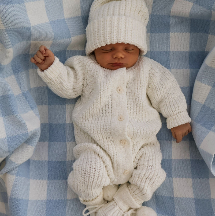 Newborn baby in a white knitted outfit and hat on a blue checkered blanket