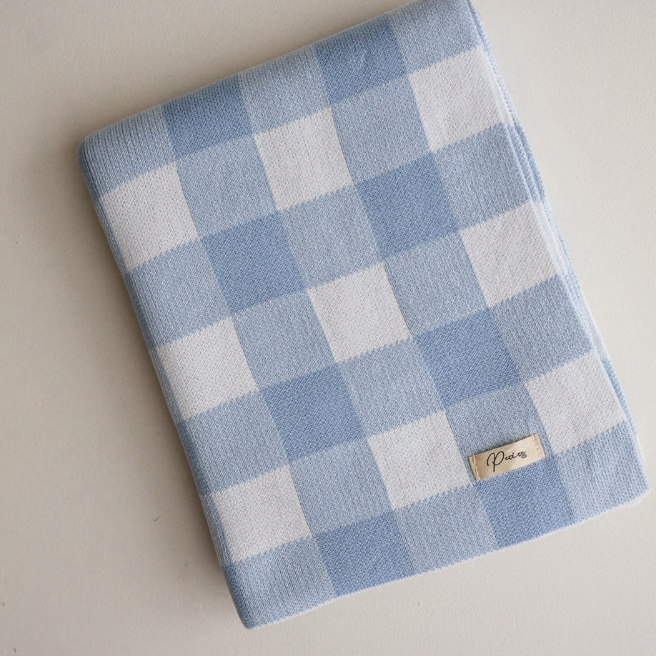 Blue and white checkered blanket with a brand label on a light gray background