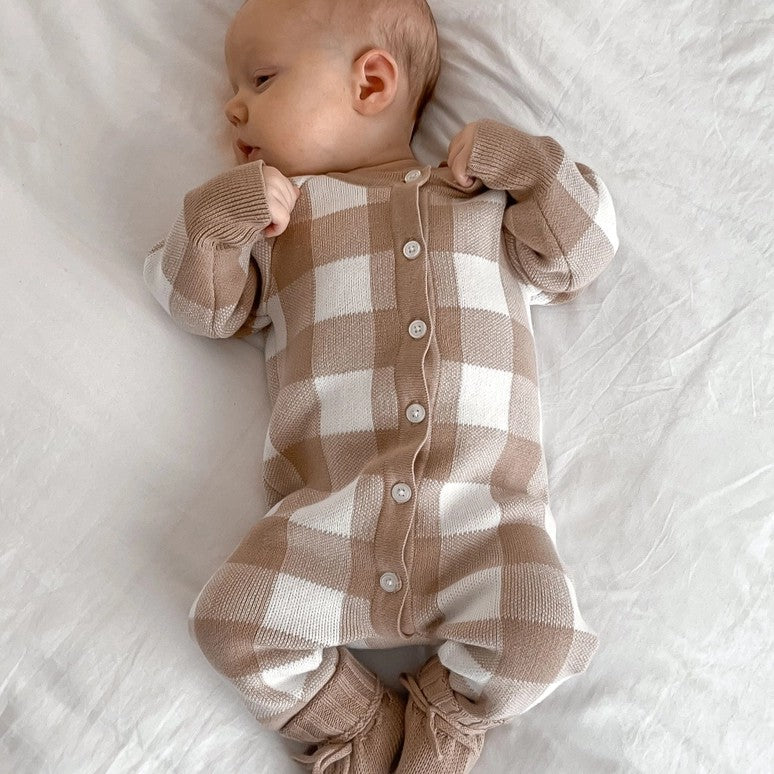 Baby wearing a brown and white checkered onesie on a white background