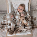 Baby lying on a checkered blanket with a teddy bear, wearing a matching outfit.