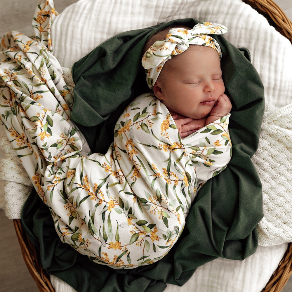 Newborn baby girl swaddled in Snuggle Hunny wrap with golden wattle designs and matching topknot from Meridian Baby