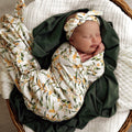 Newborn baby girl swaddled in Snuggle Hunny wrap with golden wattle designs and matching topknot from Meridian Baby
