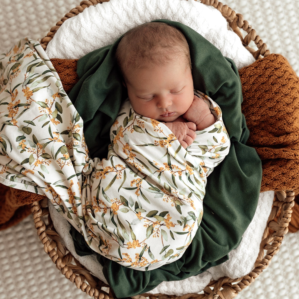 Newborn baby boy wrapped in Snuggle Hunny swaddle with golden wattle designs from Meridian Baby.