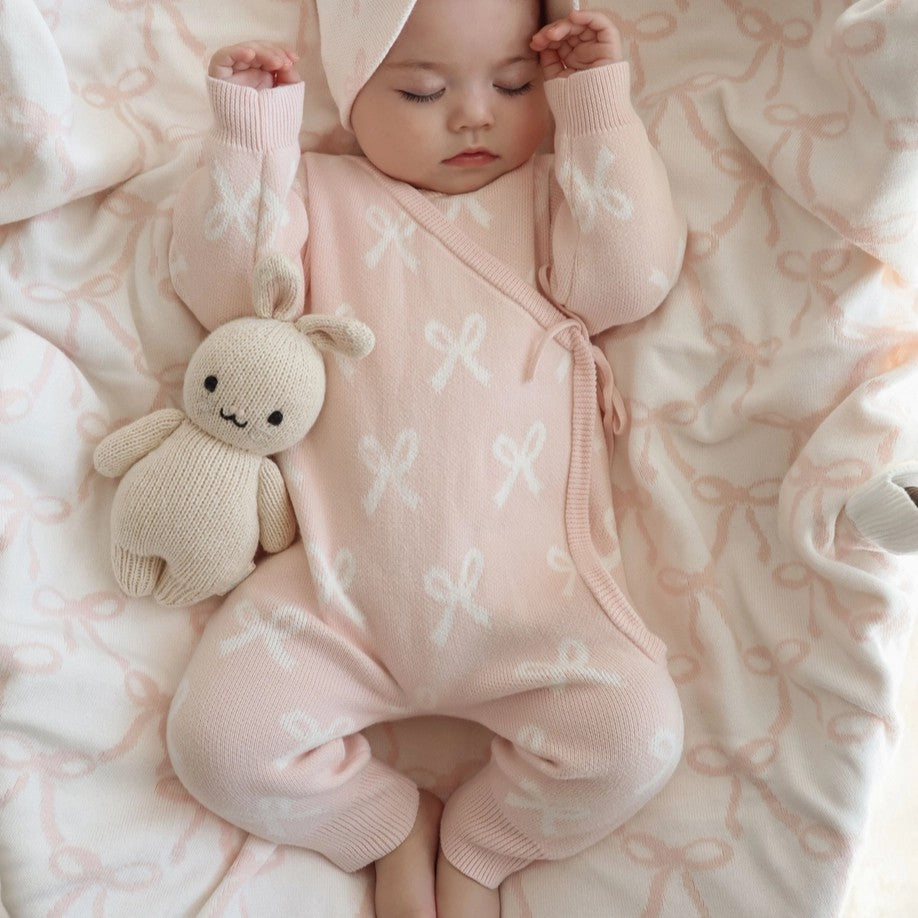 Baby in a pink outfit with a soft toy on a patterned blanket