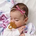 Baby with a pacifier and pink headband lying on a soft surface