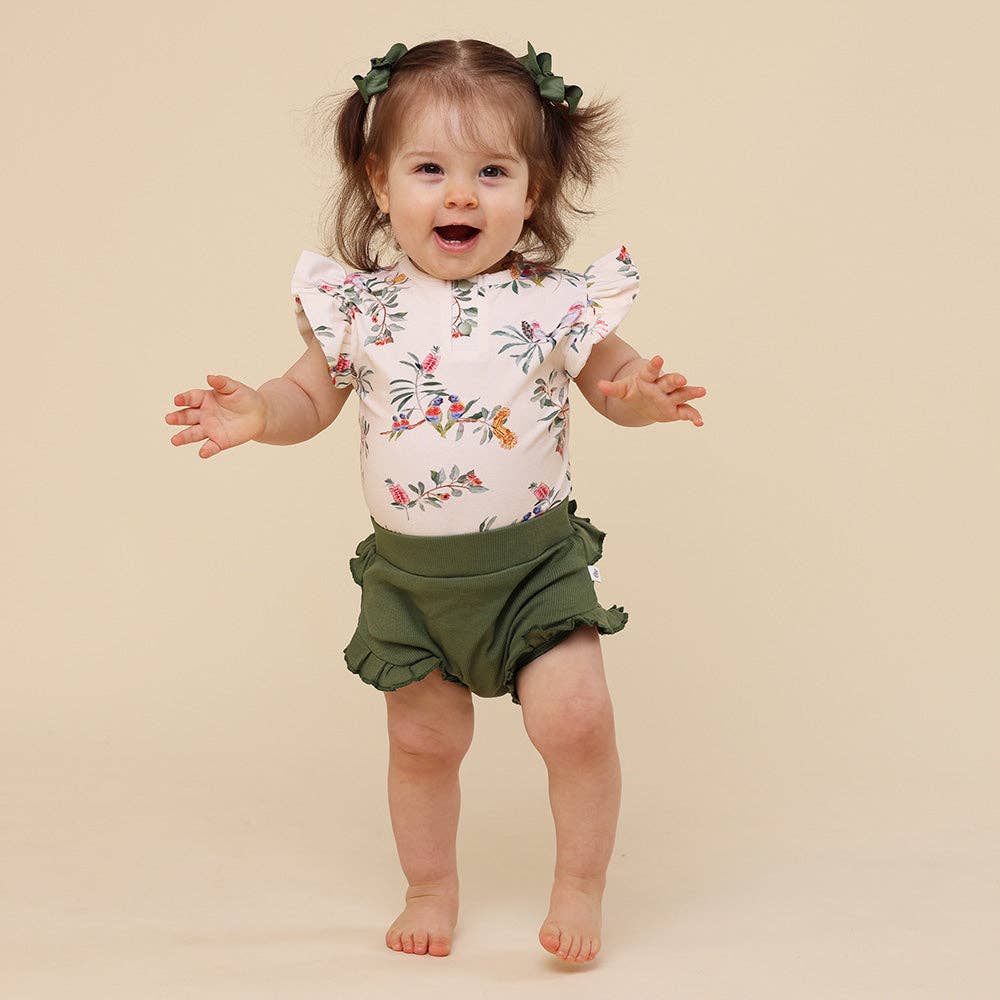 Baby wearing a floral top and green shorts with a plain background