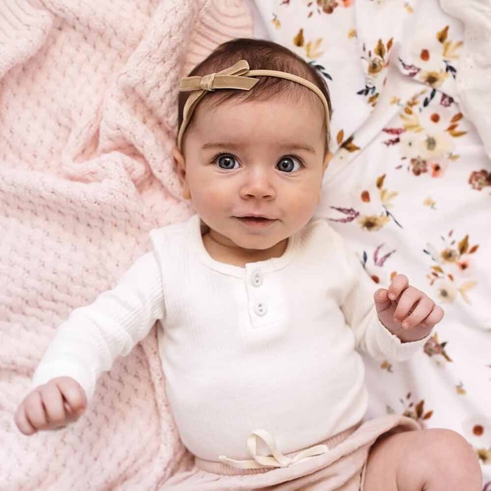 Baby wearing a white onesie and beige headband on a floral blanket
