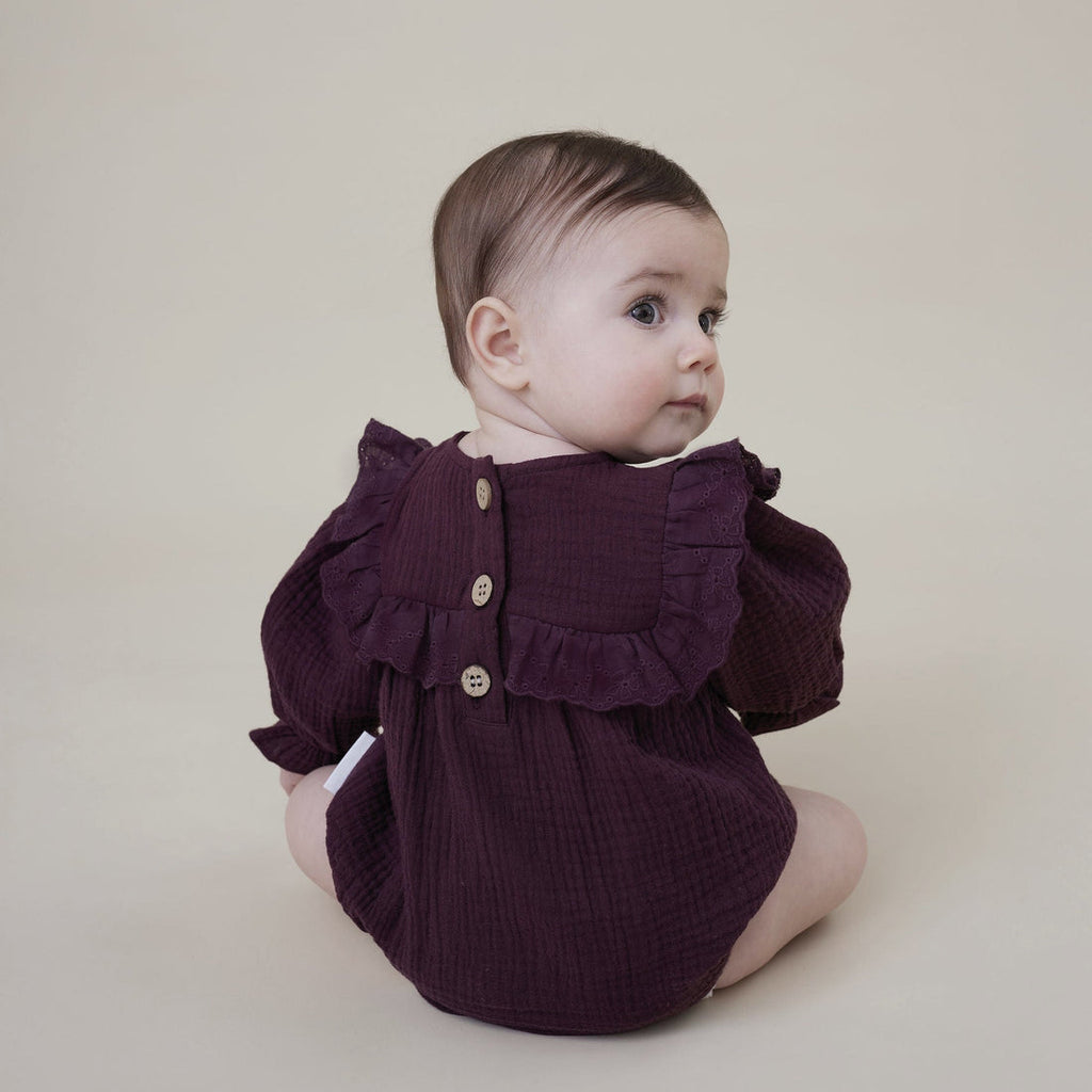 Baby girl wearing an Aster & Oak dark purple ruffled romper from Meridian Baby