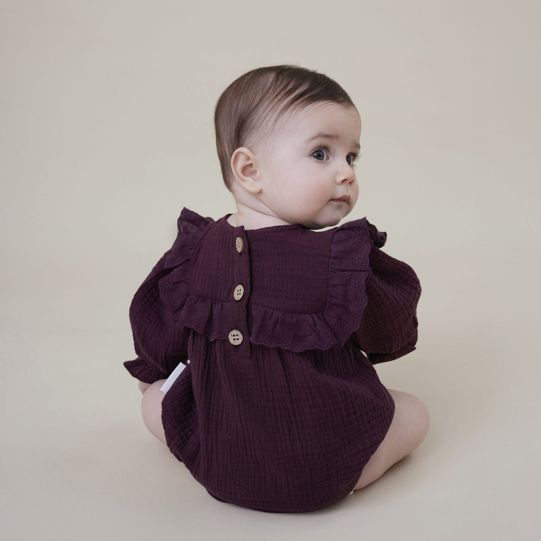 Baby wearing a dark purple ruffled romper on a plain background