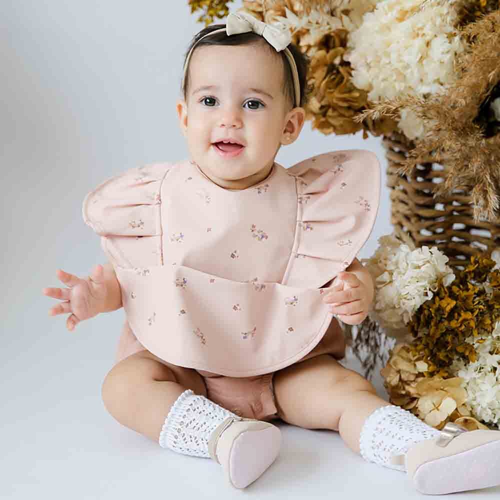Baby girl wearing Snuggle Hunny pink floral frill feeding bib from Meridian Baby