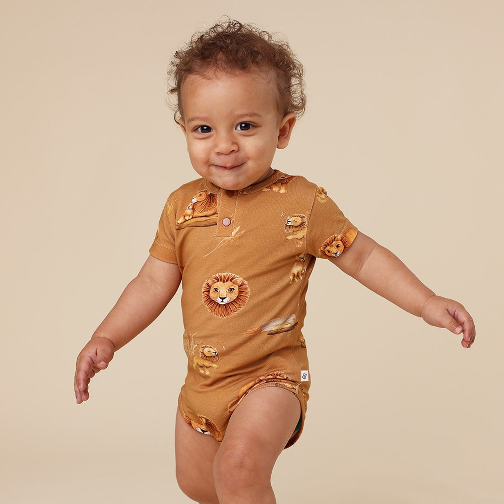 Baby wearing a brown onesie with lion prints on a beige background