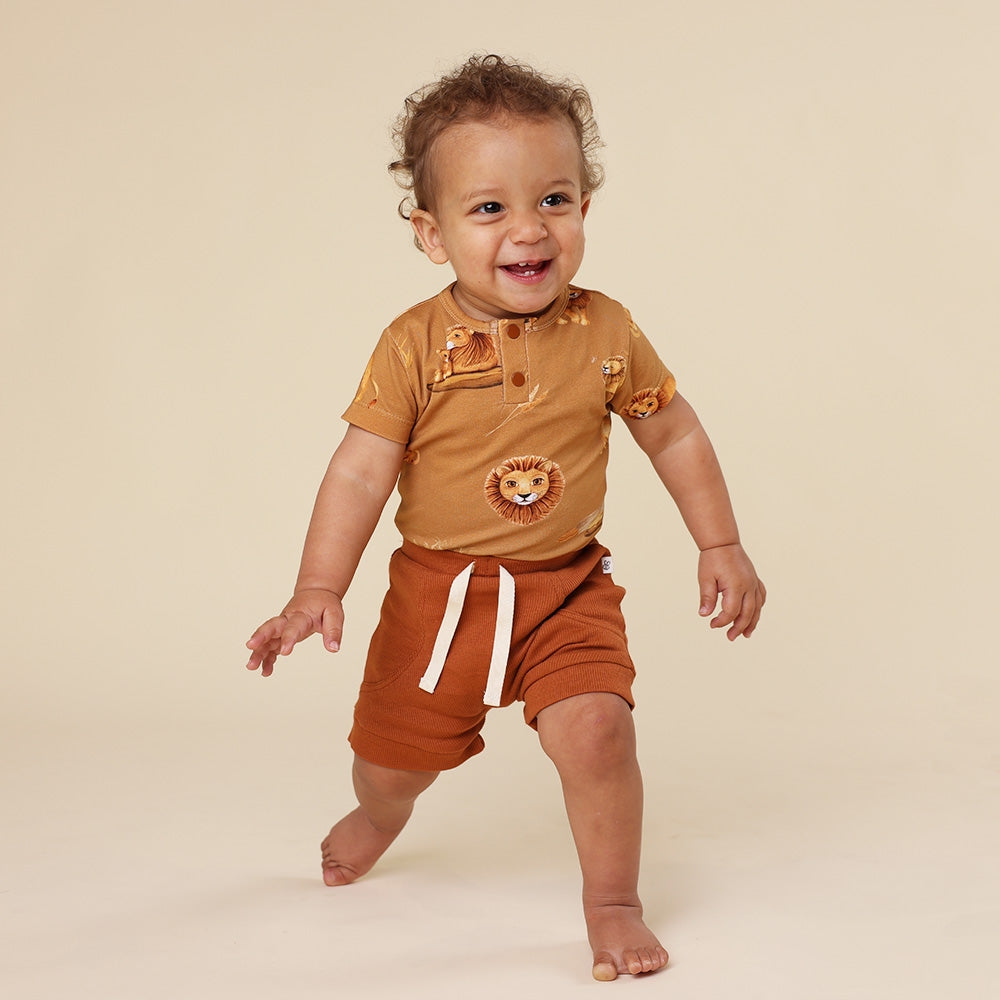 Baby wearing a brown outfit with lion designs on a beige background