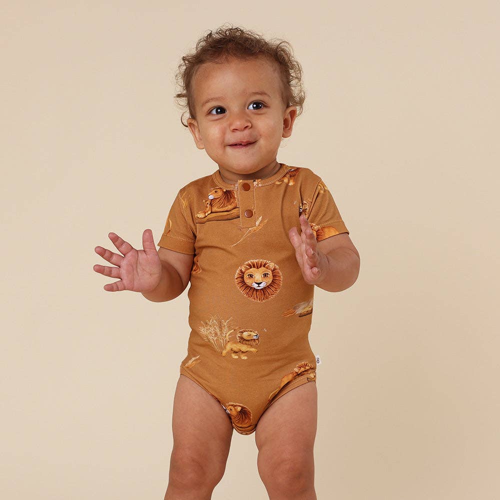 Baby wearing a brown onesie with lion prints on a beige background